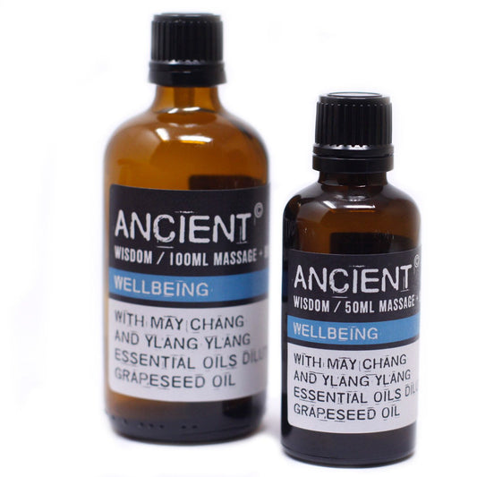 Two amber massage oil bottles stand side by side on a white background; label text: ANCIENT © WISDOM / 100ML MASSAGE + WELLBEING WITH MAY CHANG AND YLANG YLANG ESSENTIAL OILS DILUTED IN GRAPESEED OIL; ANCIENT © WISDOM / 50ML MASSAGE + WELLBEING WITH MAY CHANG AND YLANG YLANG ESSENTIAL OILS DILUTED IN GRAPESEED OIL