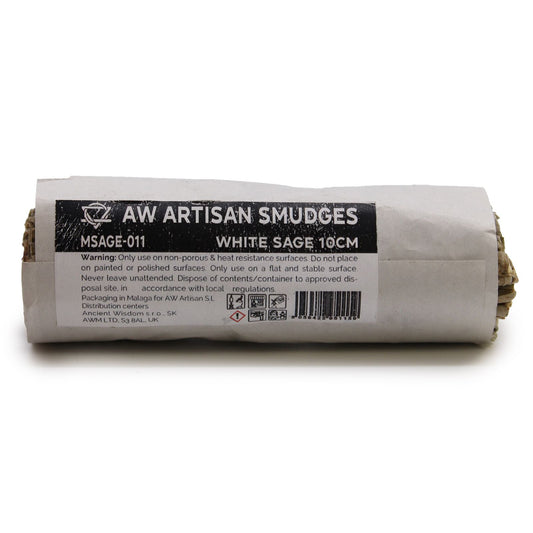 White sage smudge stick rests wrapped in a paper label on a white surface; label text: AW ARTISAN SMUDGES MSAGE-011 WHITE SAGE 10CM Warning: Only use on non-porous & heat resistant surfaces. Do not place on painted or polished surfaces. Only use on a flat and stable surface. Never leave unattended. Dispose of contents/container to approved disposal site in accordance with local regulations. Packaging in Malaga for AW Artisan S.L Distribution centers Ancient Wisdom s.r.o., SK AWM LTD, S3 8AL, UK