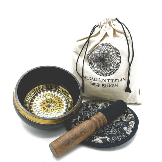 Tibetan singing bowl sits with a wooden striker and brocade pad beside a drawstring bag labeled "MEDALLION TIBETAN Singing Bowl" on a white background.