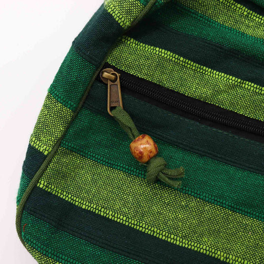 Green striped fabric pouch showing a black zipper with bronze pull stamped SUN, a tied green cord and a small carved wooden bead against a white background.
