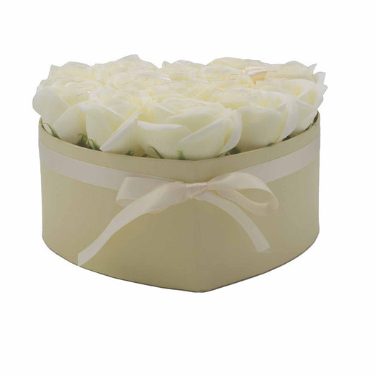 Heart-shaped cream box holds a tight arrangement of white roses, tied with a matching satin ribbon, photographed against a plain white background.