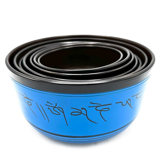 Set of nested metal bowls stacked inside each other on a white background, blue exterior decorated with black Tibetan script reading "Om mani padme hum".
