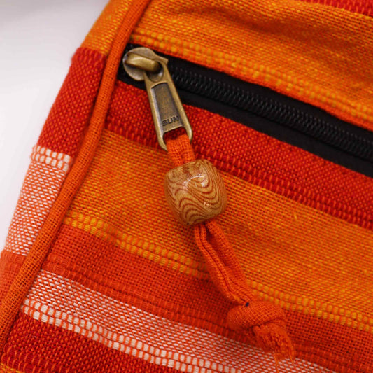 Zipper pull with "SUN" stamped on brass is attached to an orange fabric cord ending in a wooden bead on a striped orange and white woven pouch.