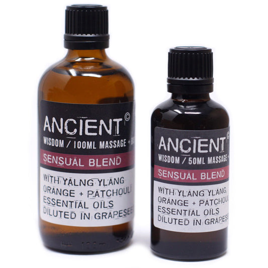 Two amber glass massage oil bottles stand side by side on a white background; labels read ANCIENT © WISDOM / 100ML MASSAGE +; ANCIENT © WISDOM / 50ML MASSAGE; SENSUAL BLEND; WITH YLANG YLANG ORANGE + PATCHOULI ESSENTIAL OILS DILUTED IN GRAPESEED.