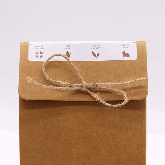 Kraft paper pouch bound by a frayed twine bow, set against a pale neutral background, MADE IN ENGLAND HAND MADE VEGAN FRIENDLY CRUELTY FREE
