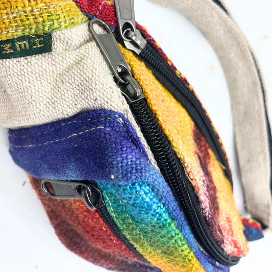 Small multicolored woven pouch with three metal zipper pulls along a black zipper, fabric handle to the right, textured panels of purple, turquoise, yellow and red on white background; tag reads ZMI.