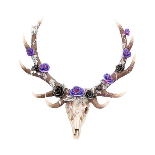 A deer skull with antlers is adorned with decorative purple and black roses, creating an artistic and mystical appearance against a plain white background.