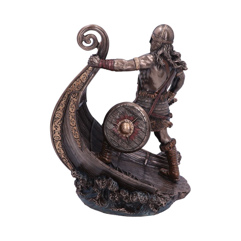 A bronze-colored Viking figurine stands on a ship, holding a decorative shield, surrounded by detailed carvings and waves, evoking a historical, adventurous setting.
