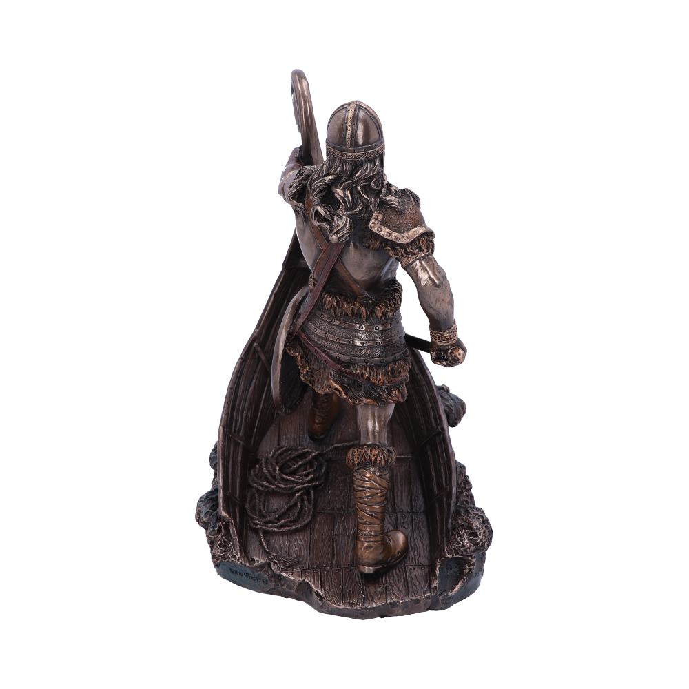 A bronze-colored statue of a Viking warrior stands on a wooden ship deck, holding a shield and rope, with detailed armor and flowing hair, suggesting readiness for battle.