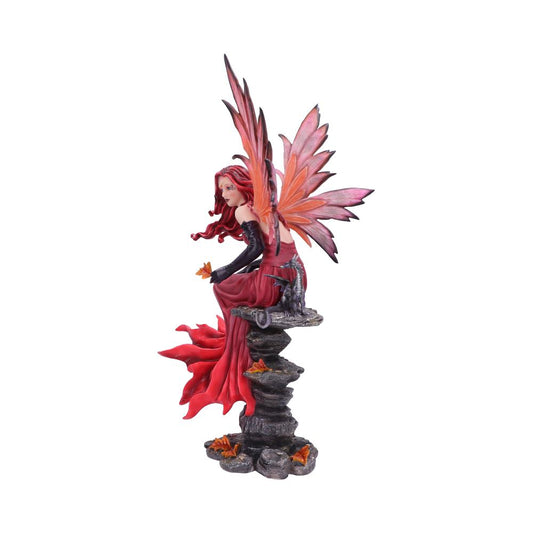 A winged fairy sits, holding a small flower. The fairy is wearing a red dress, sitting upon a small stack of rocks. A dragon sculpture also sits on the rock.