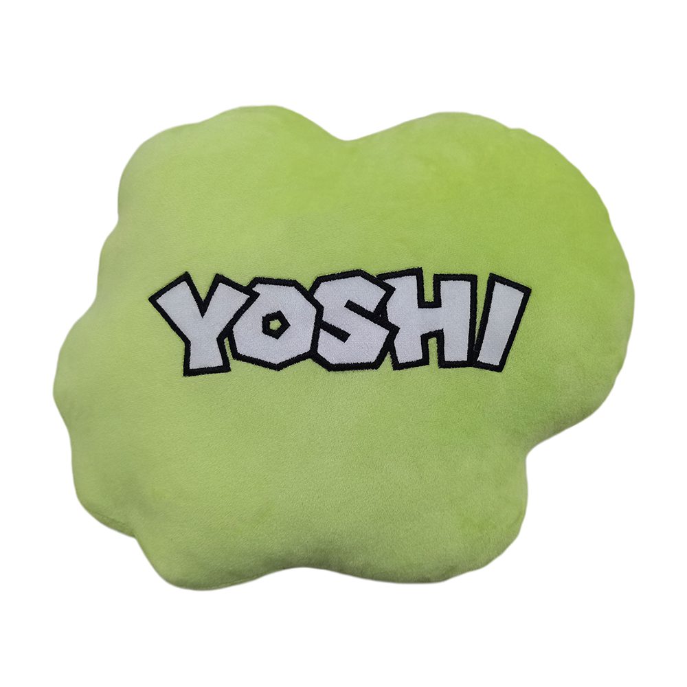 A green, cloud-shaped pillow features the bold text "YOSHI" in white, outlined in black, centered on the surface against a plain white background.