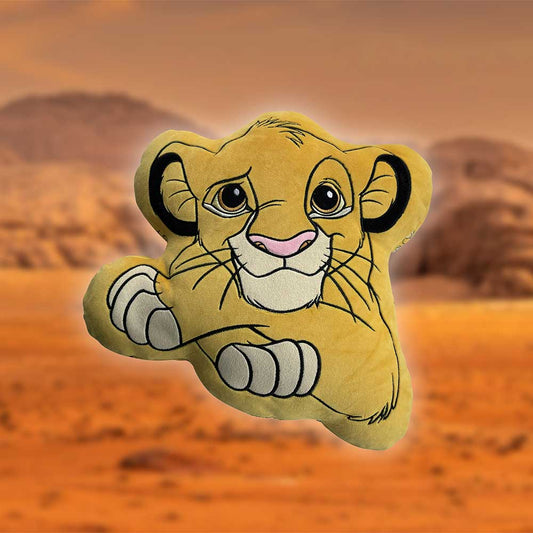 A yellow plush Simba pillow sits in front of a blurred, sandy orange savanna landscape.