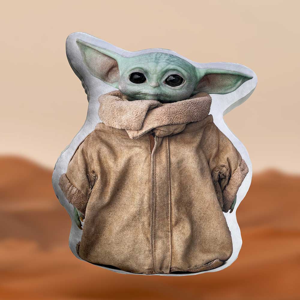 A green, big-eared character stands still, wearing a brown robe. It appears on a pillow with a desert-like background, giving a sense of isolation and simplicity.