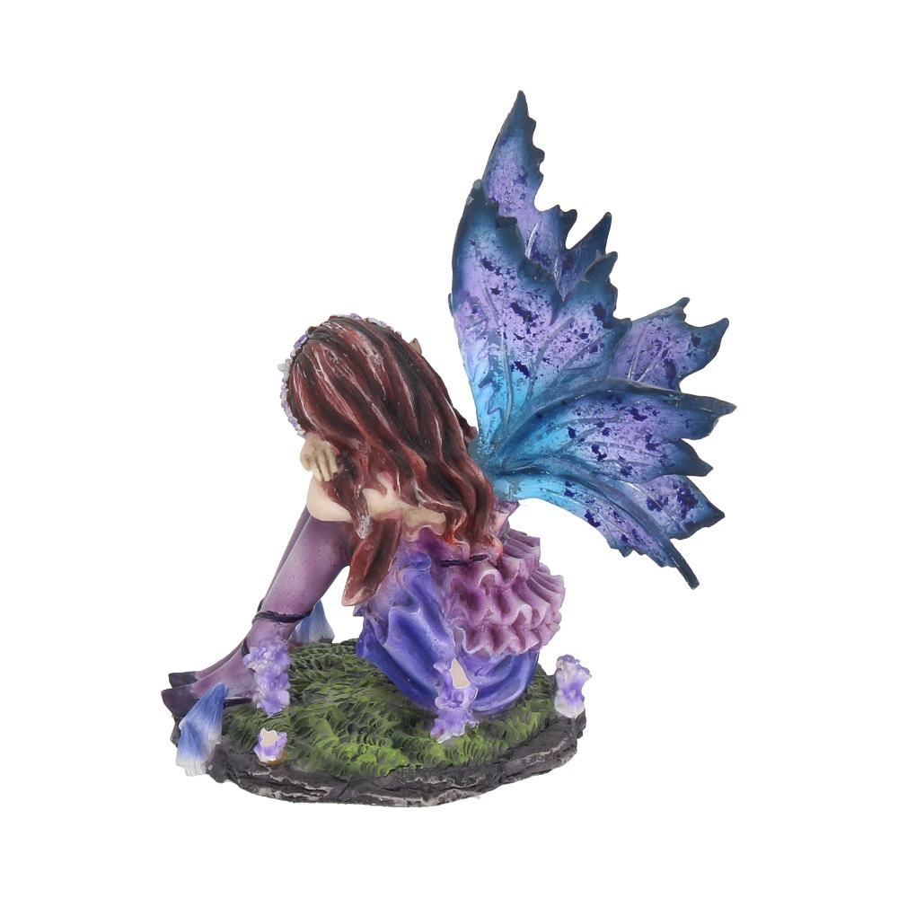 A fairy figurine sits pensively, resting its head on its knees. It has vibrant blue wings and purple attire, placed on a grassy base adorned with small purple flowers.