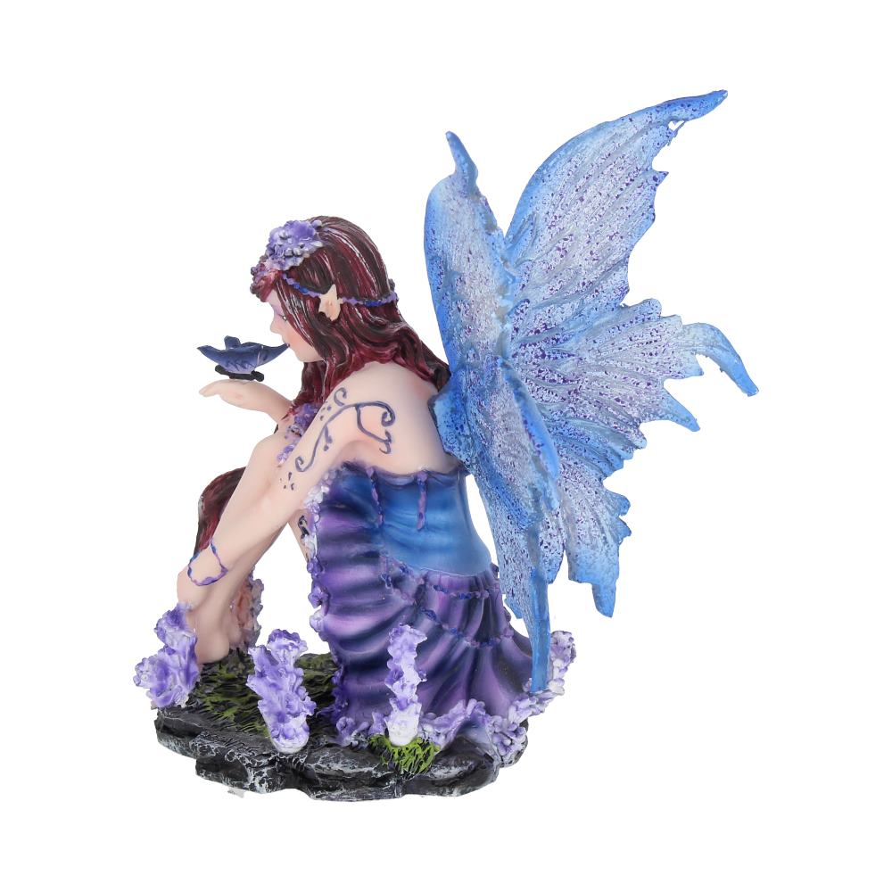 A fairy with blue wings and purple attire kneels, holding a butterfly on her hand, surrounded by violet flowers on a rocky base.