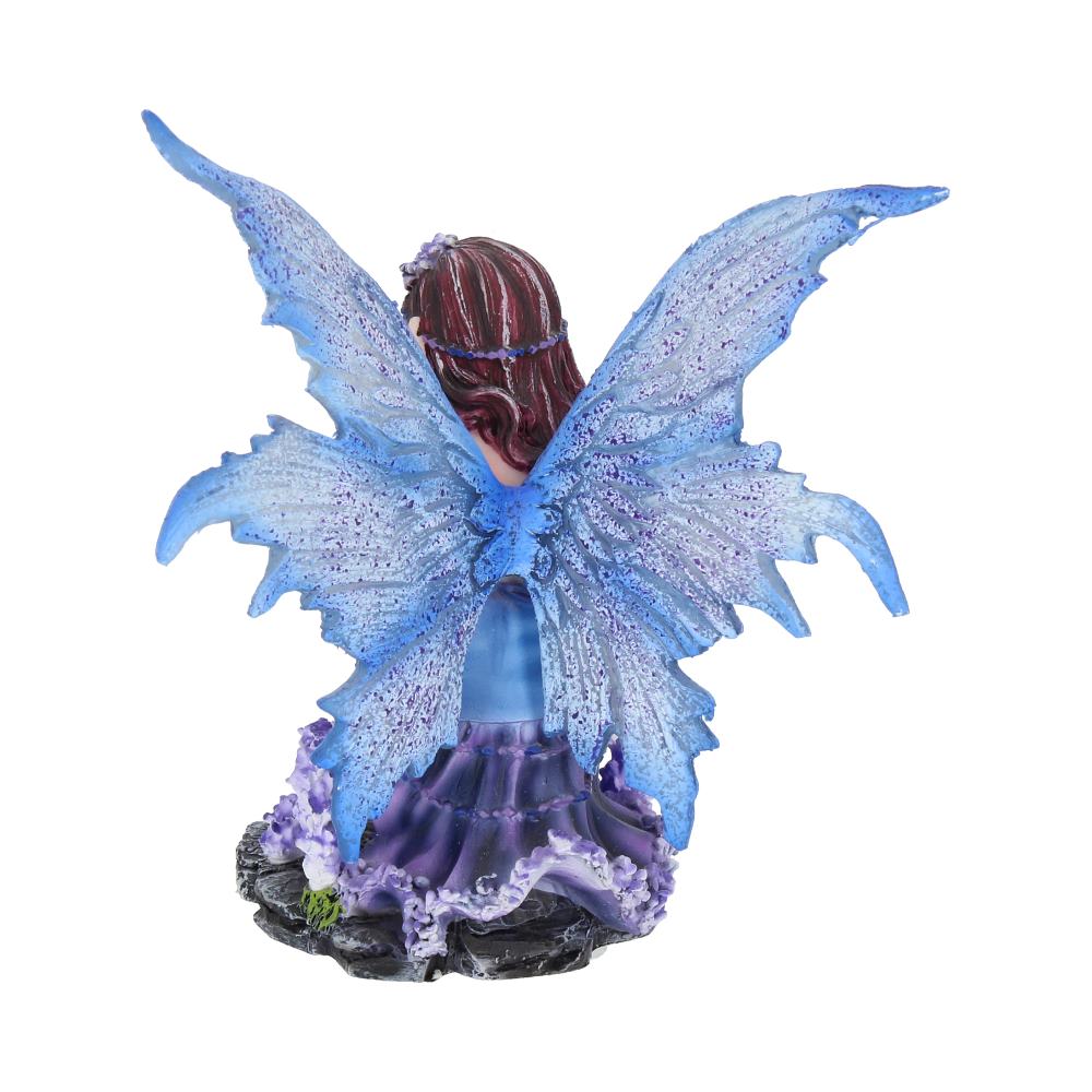 A fairy figurine with blue wings sits on a black and purple base, facing away. The fairy has brown hair and a purple dress, set against a plain white background.