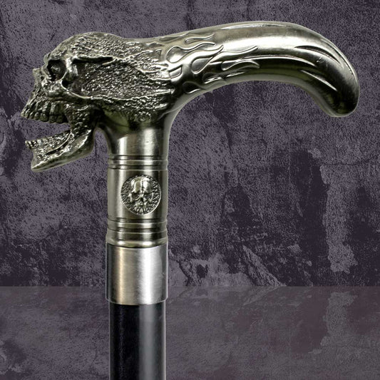 A metallic cane handle shaped like a roaring skull, adorned with flame engravings and a medallion, stands against a textured dark background.