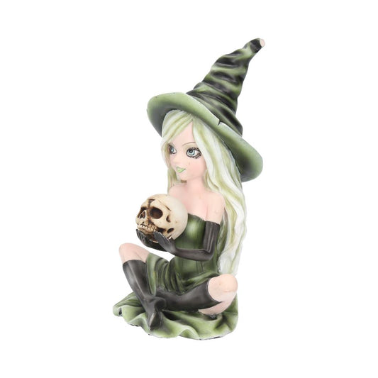A small figurine of a sitting witch with long hair, wearing a pointed hat, holds a skull. The witch features intricate details in her expression and clothing, set against a plain backdrop.