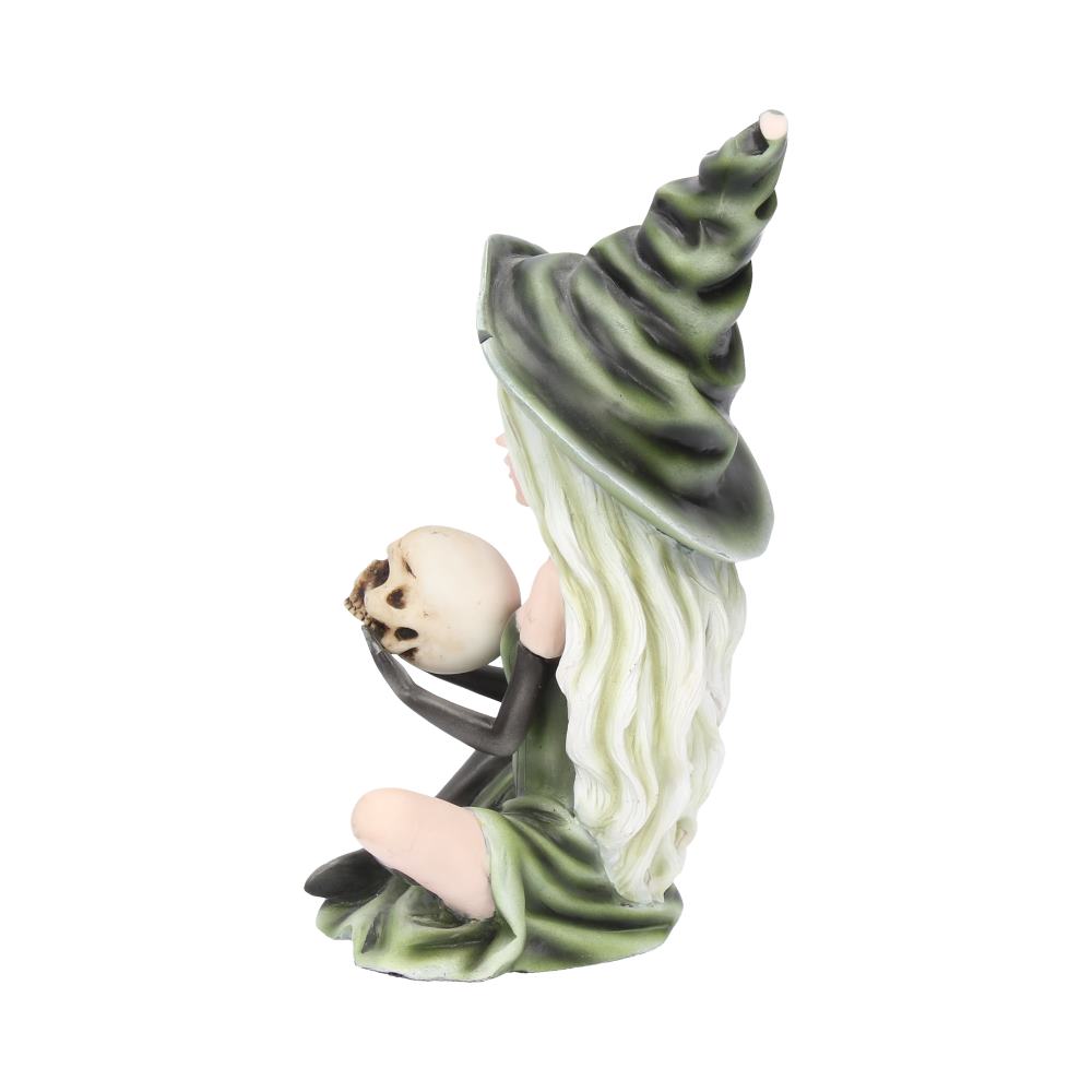 A figurine of a witch with long hair holds a small skull in one hand. She wears a green, pointed hat and matching dress, sitting against a plain white background.