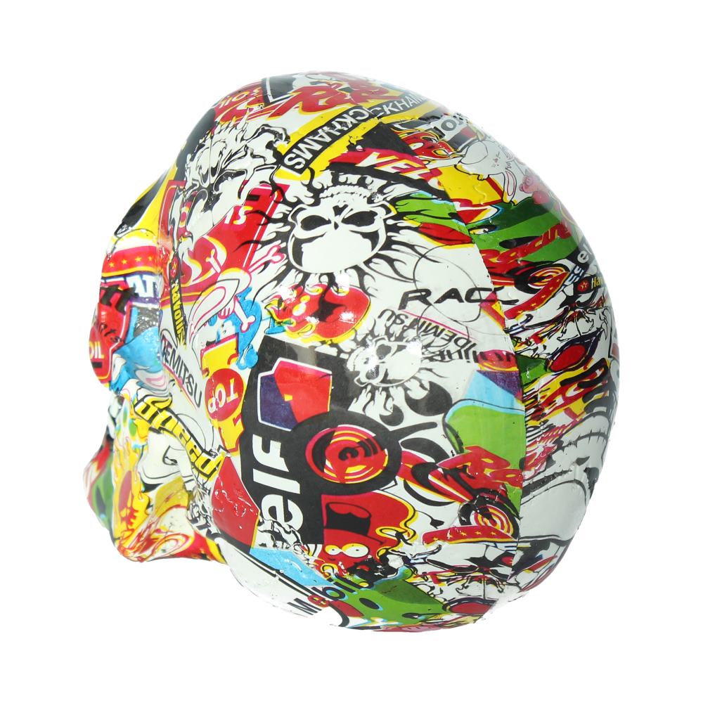A skull-shaped object is wrapped in a colorful collage of various stickers and graphics, featuring bold text and vibrant patterns, set against a plain white background.