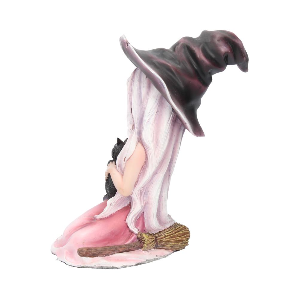 A figurine of a witch wearing a tall, floppy hat and long dress kneels, cradling a black cat. A broom lies beside her, set against a plain, white background.