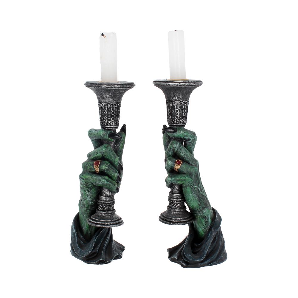 Two candlestick holders, shaped like green, monstrous hands with rings, hold thin white candles. The hands emerge from draped fabric against a stark white background.