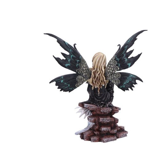 Fairy figurine with long blonde hair and ornate black and teal wings sits perched on a jagged stacked-rock ledge against a plain white background.