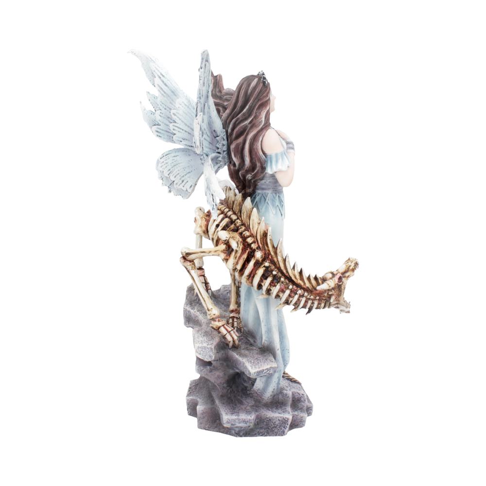 A fairy figurine with wings stands on a gray rock next to a dragon skeleton, its back turned to the viewer.