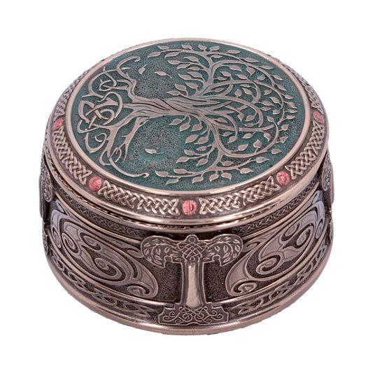 Ornate circular box displaying a Celtic tree design on the lid, surrounded by intricate patterns and red accents. The metallic surface features swirling designs, set in an artistic, decorative environment.