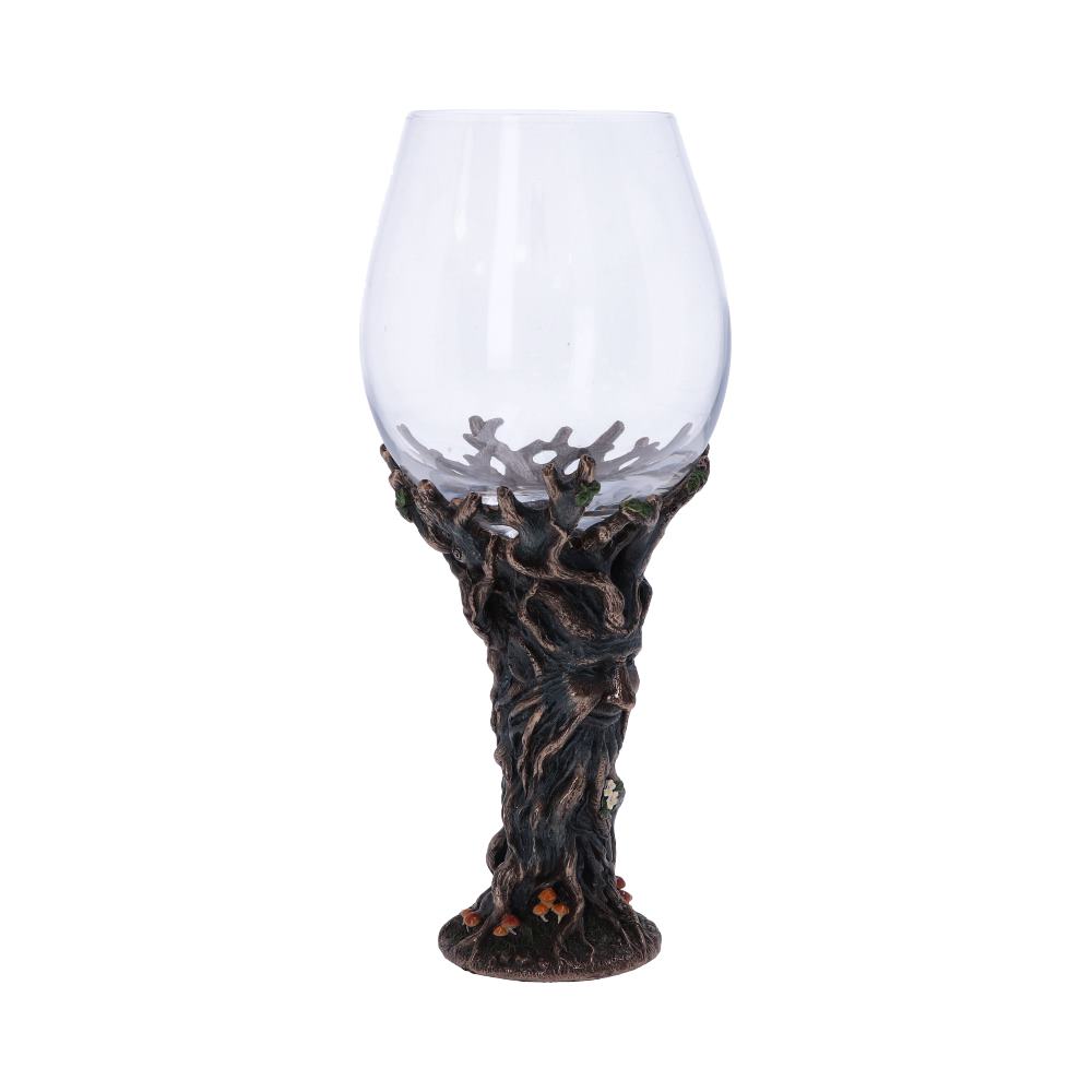 A clear wine glass is held by a dark brown tree trunk base, complete with roots, leaves, and a face. The background is plain white.