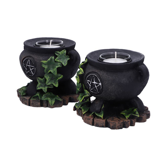Two small black cauldron candle holders hold white tealight candles while green ivy climbs their sides on textured brown stone like bases against a plain white background.