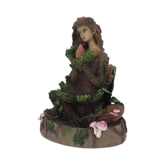 A sculpture of a tree-like woman holds an egg, surrounded by green leaves and mushrooms. The figure and base resemble a tree trunk, creating an earthy, natural setting.