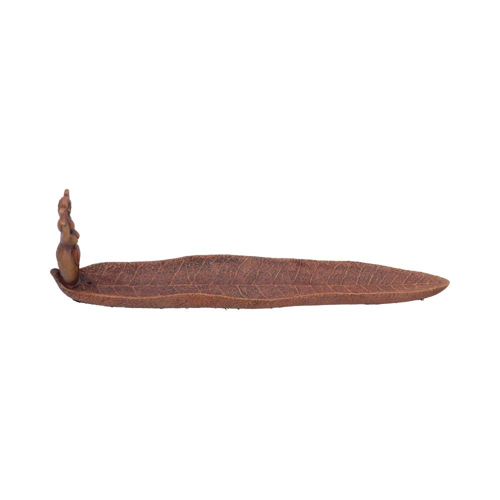 A brown leaf-shaped incense burner holds incense sticks; a small, carved figure rests at one end. It sits on a white background.