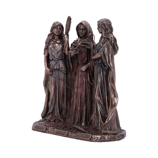 A bronze statue depicts three cloaked female figures, each holding distinct items. The base displays the names "Clotho," "Atropos," and "Lachesis." They're standing together, possibly symbolizing mythology.