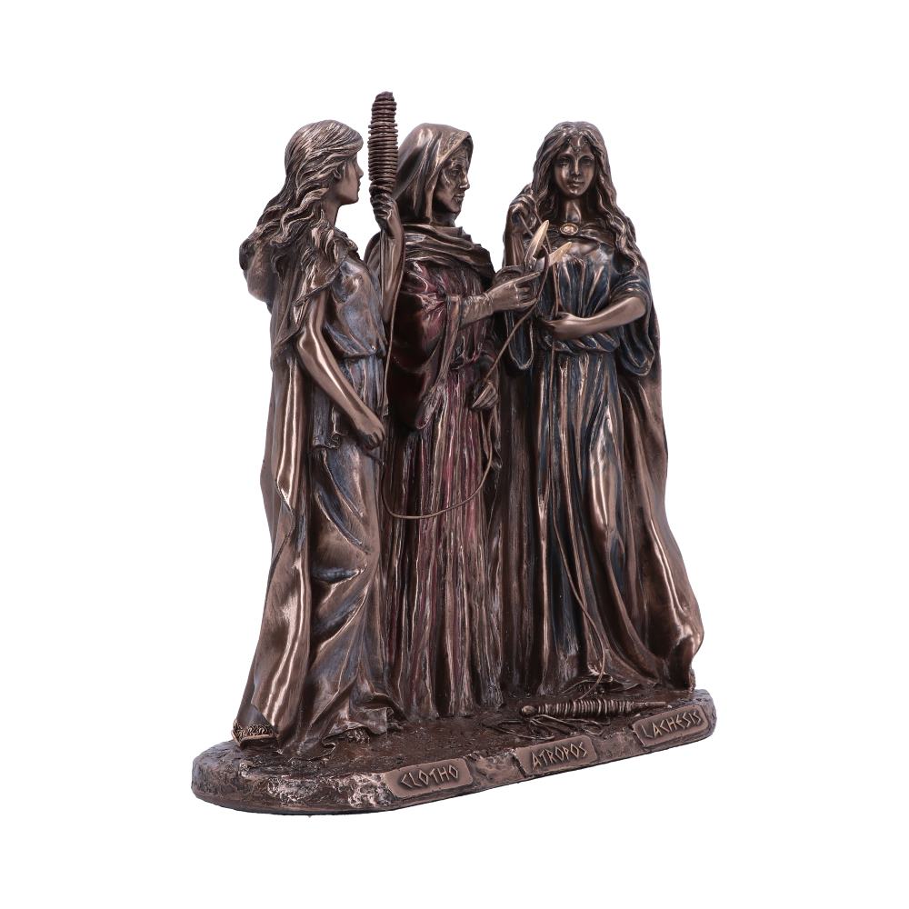A bronze statue of three women stands together, each dressed in flowing robes, holding symbolic items. The base of the statue reads: "CLOTHO," "ATROPOS," "LACHESIS."