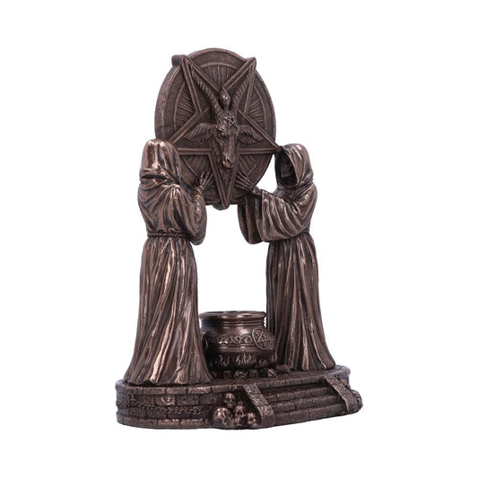 A bronze-colored statue shows two robed figures holding a pentagram with a goat's head. The statue is on a base with skulls and a cauldron.