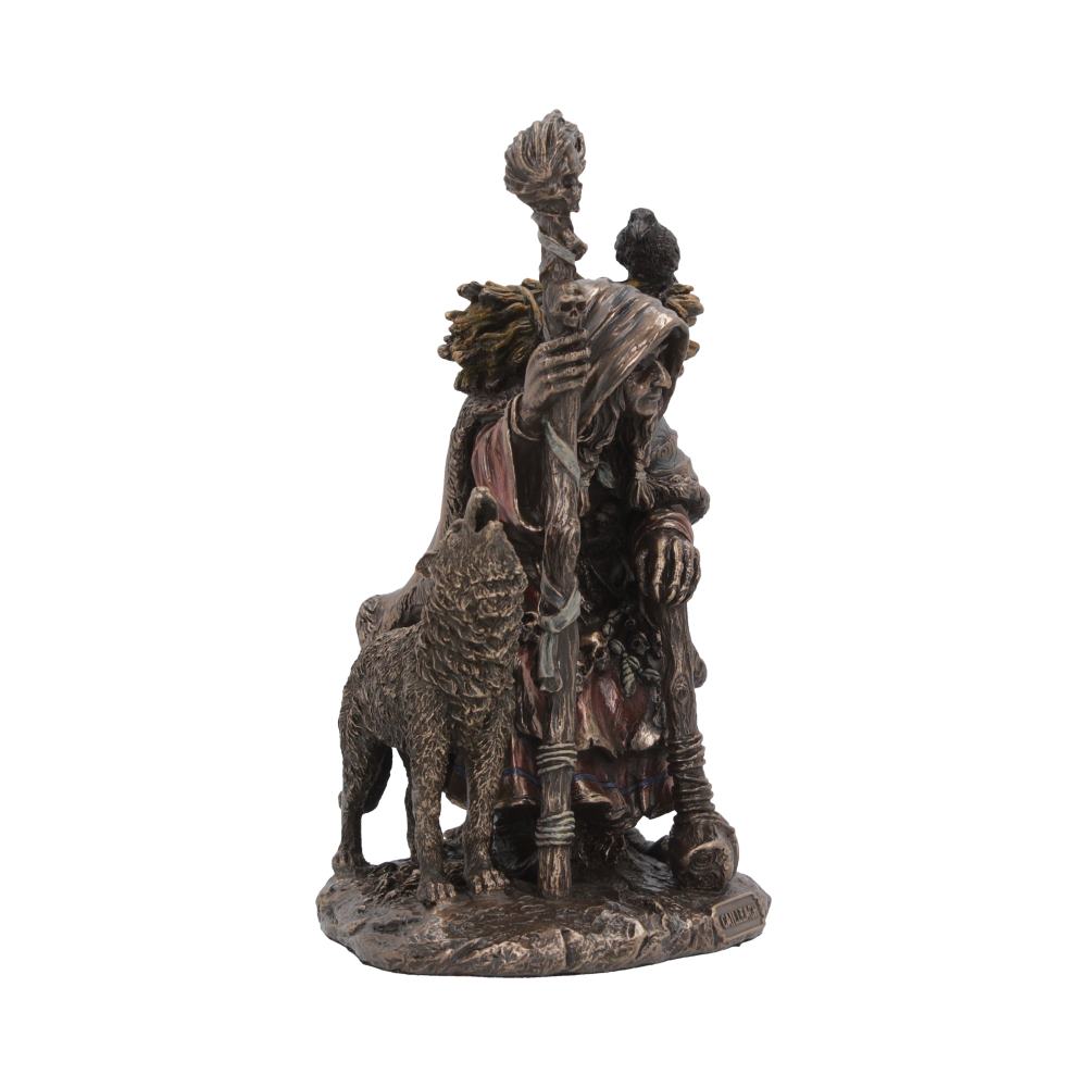 A bronze figurine depicts an elderly hooded figure holding a staff, with a crow perched on their shoulder and a sheep by their side, resembling a mystical or pastoral character.