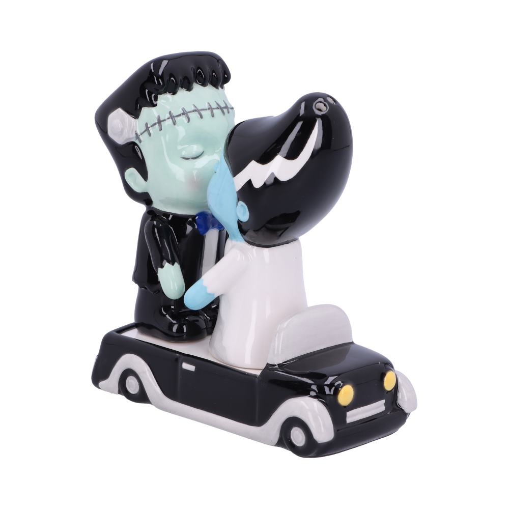 Two ceramic figurines of Frankenstein and his bride kiss atop a black car. Both figures are cartoonish, the bride wears a white dress, and the groom wears a suit with a bow tie.