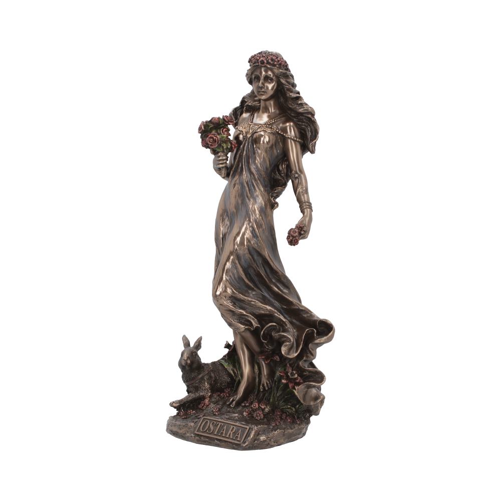 A bronze statue depicts a woman holding flowers, wearing a flowing dress with a floral crown. A rabbit is at her feet. The base reads "OSTARA."