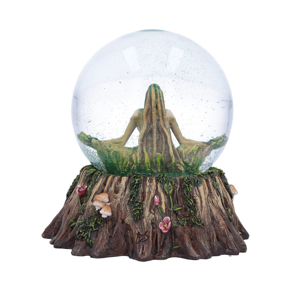 A snow globe depicts a figure seated in a meditative pose, nestled within a tree-trunk base adorned with flowers and mushrooms.