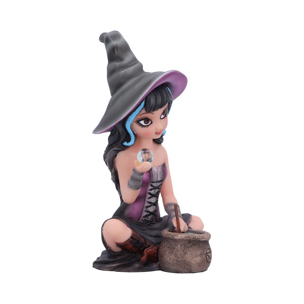 A figurine of a young witch, wearing a purple dress and tall hat, holds a crystal ball and stirs a cauldron. The scene is isolated on a white background.