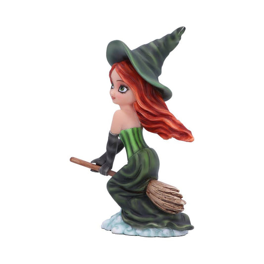 A figurine of a young witch is perched on a broomstick, wearing a green dress and hat, with flowing red hair, set against a plain white background.
