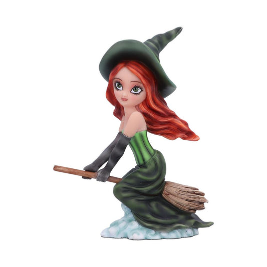 A figurine of a young witch rides a broomstick. She has long red hair, a green dress, and a pointed hat, with a cloudy base below her, against a plain backdrop.