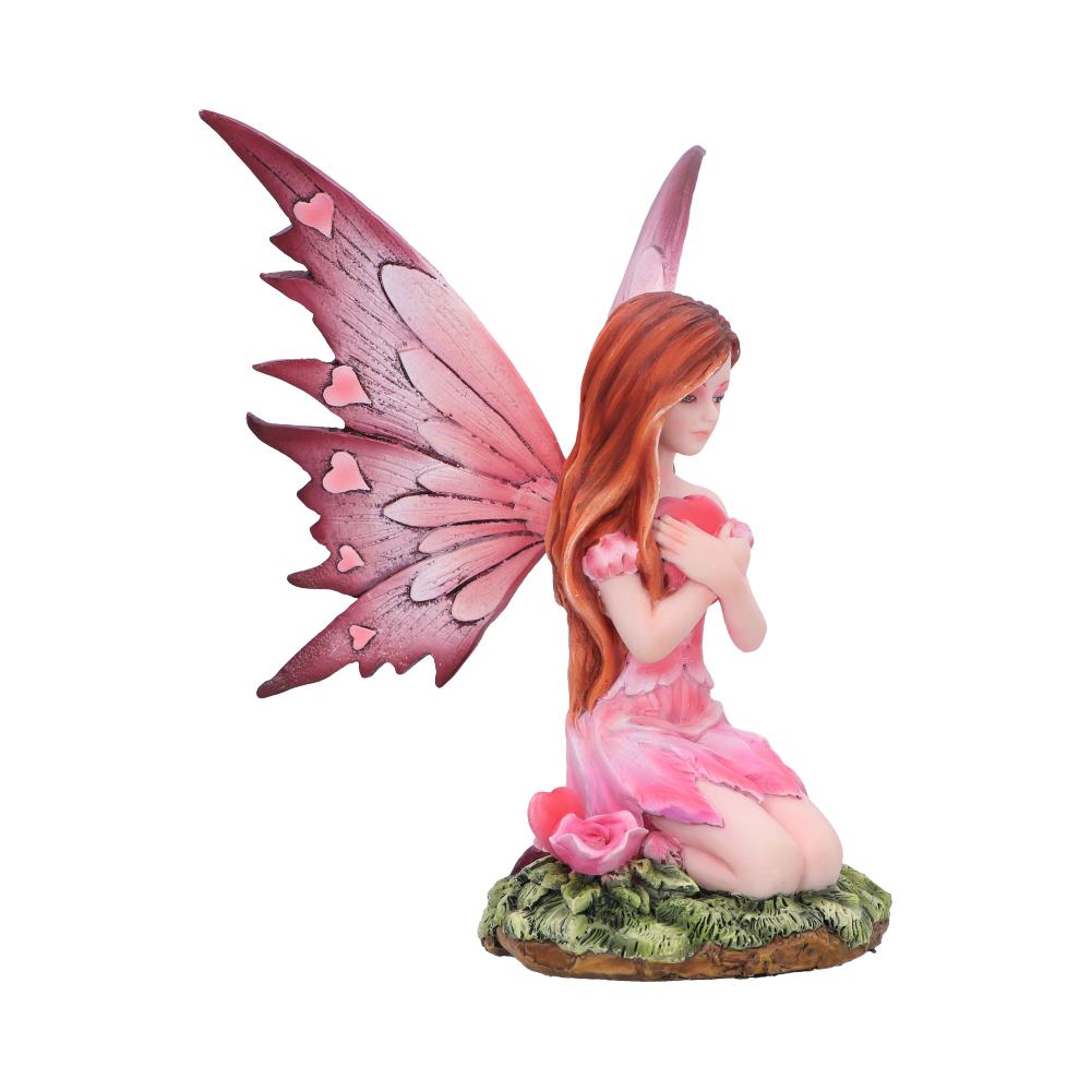 A fairy with heart-shaped wings kneels on a mossy patch, clutching a red heart to her chest with both arms. A pink rose is at her side.