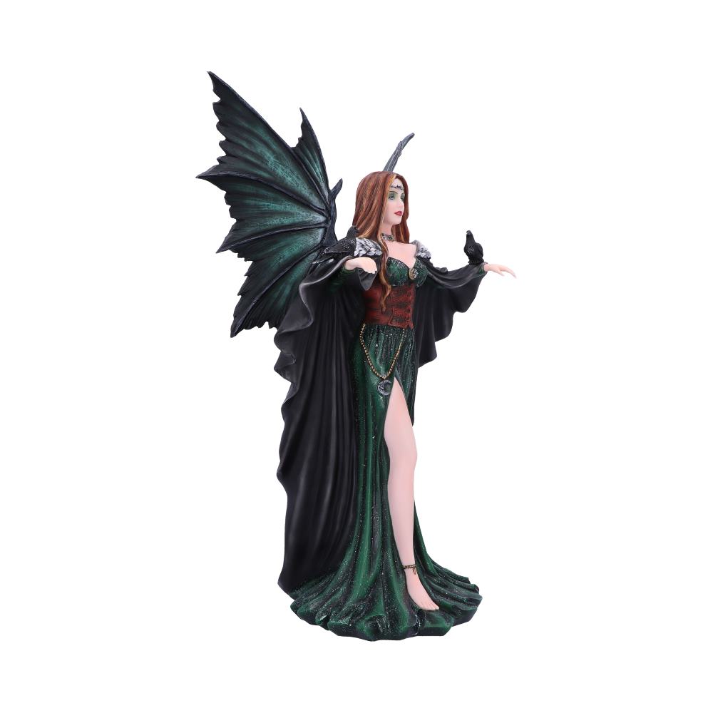 A fairy figurine stands, adorned in a dark green gown and black cape, with outstretched arm, a small, black bird perched on her hand. The background is plain white.