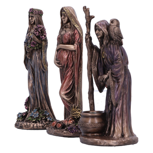 Three bronze-colored female statues stand, each representing a different stage of life: Maiden with flowers, Mother with child, and Crone with owl, all on decorative, botanical bases.