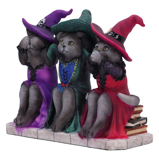 Three cat sculptures dressed as witches, each in different colored robes and hats, mimic "see no evil, hear no evil, speak no evil," sitting on a stone-like base beside stacked books.