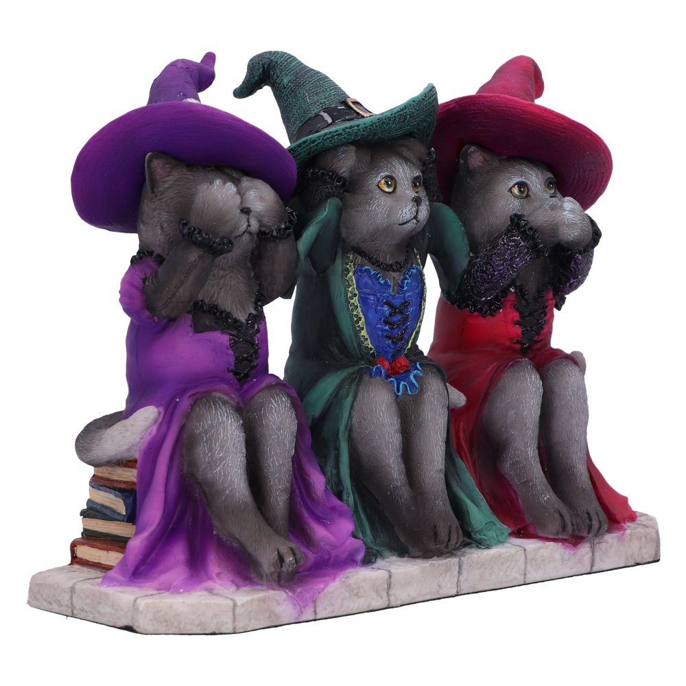 Three gray cat figurines, dressed in colorful witch outfits, pose with "see no evil, hear no evil, speak no evil" gestures, sitting on stone tiles. The left cat rests on books.