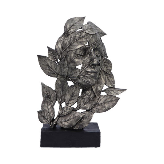 A metallic sculpture features leaves intricately arranged to form a human face. It stands on a rectangular black base, highlighting the artistic blending of nature and humanity in a minimalist setting.