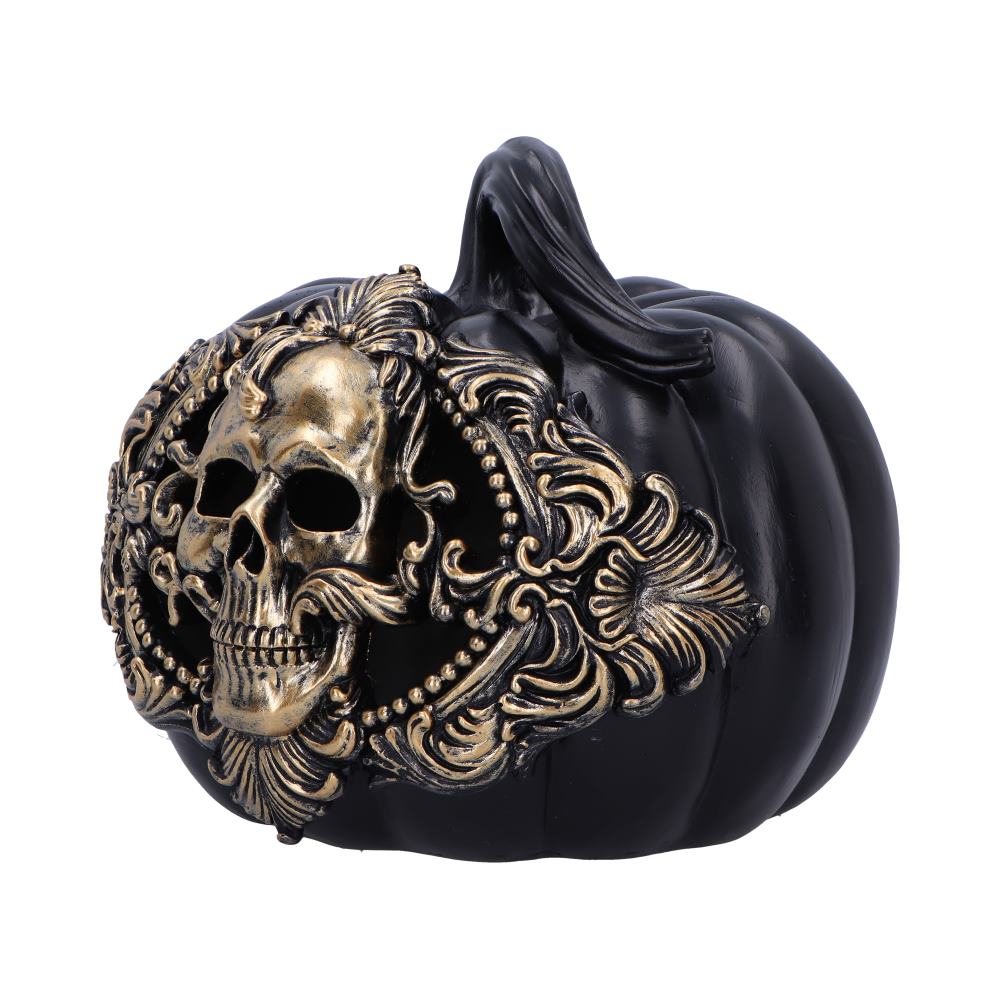 A black pumpkin adorned with an ornate gold skull design is placed on a white background, emphasizing its decorative details.
